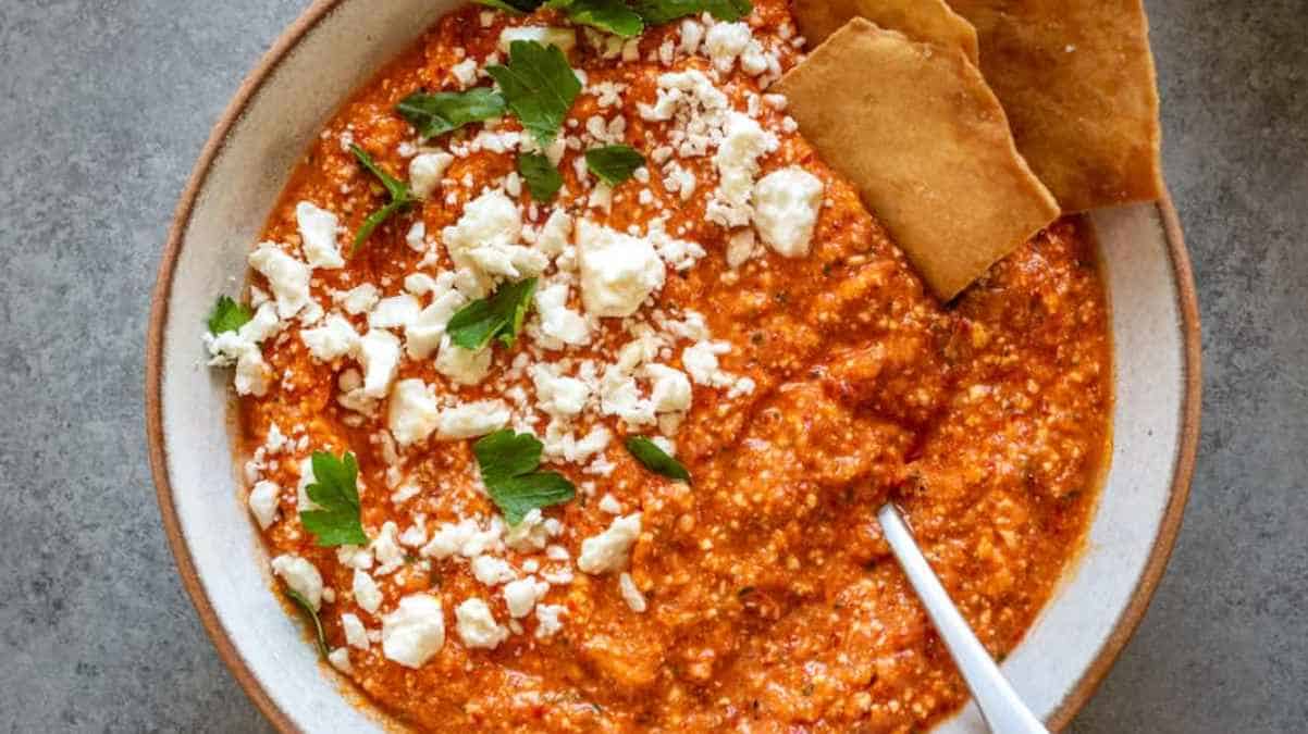 A bowl of hummus with pita bread and feta cheese.