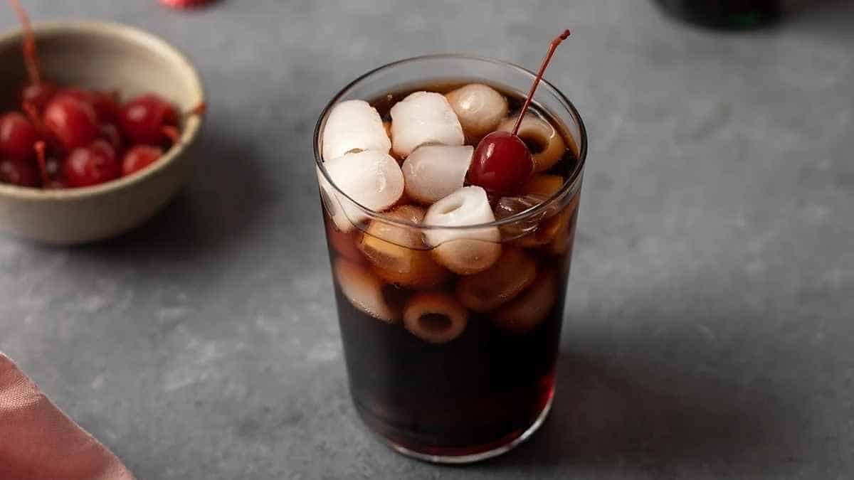 A glass of cola with cherries and ice in it.
