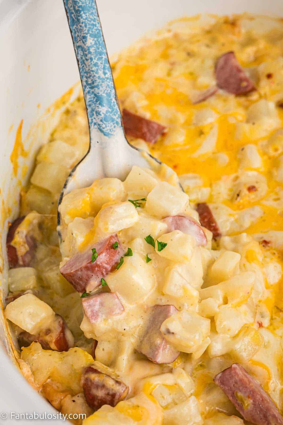 A spoonful of potato and ham casserole in a crock pot, perfect for sausage lovers.