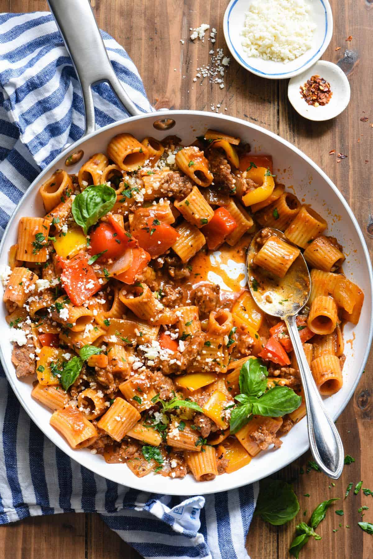 Ground sausage pasta with vegetables in a skillet on a wooden table.