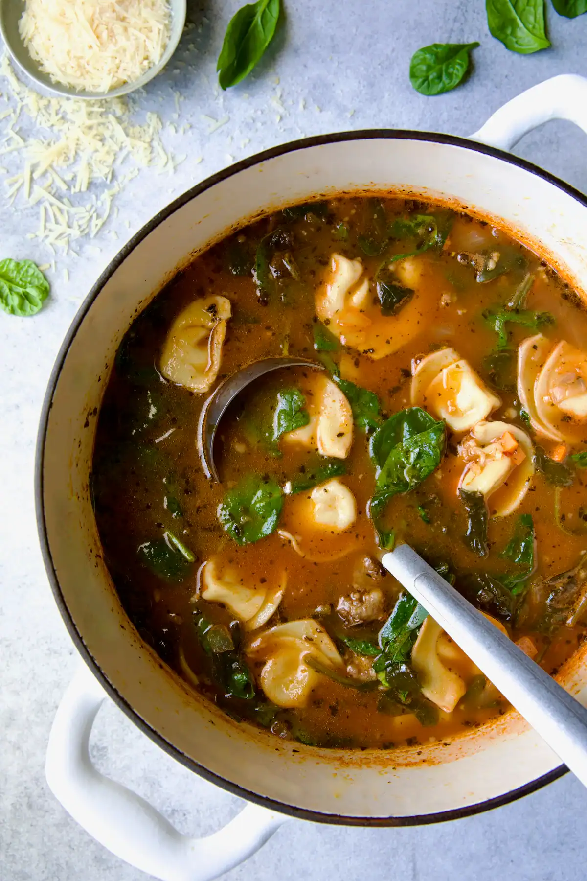 A bowl of soup with tortellini, spinach, and ground sausage.