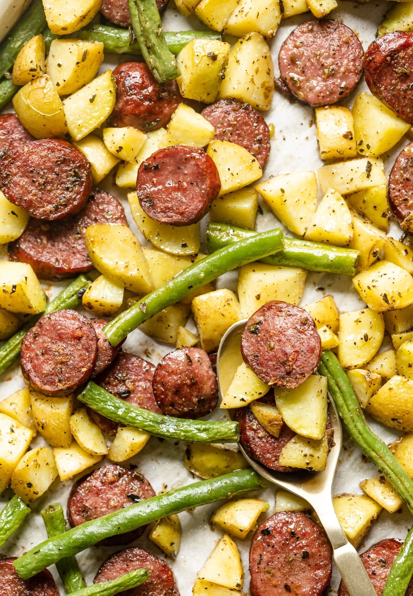 Sausage, potatoes, and green beans all baked together on a single sheet.