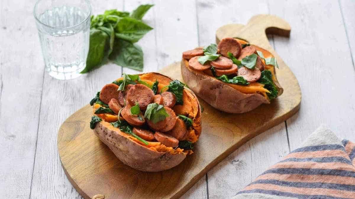 Two sweet potatoes with sausage and spinach on a wooden cutting board.