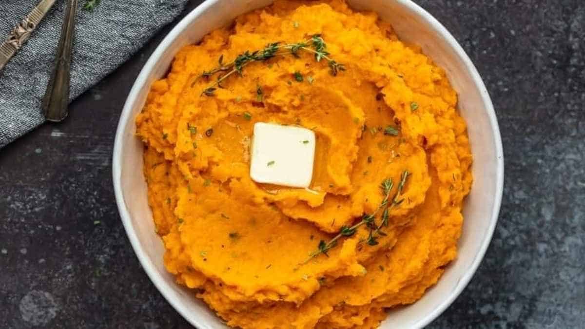 A bowl of sweet potato mashed potatoes with butter and sprigs of thyme.