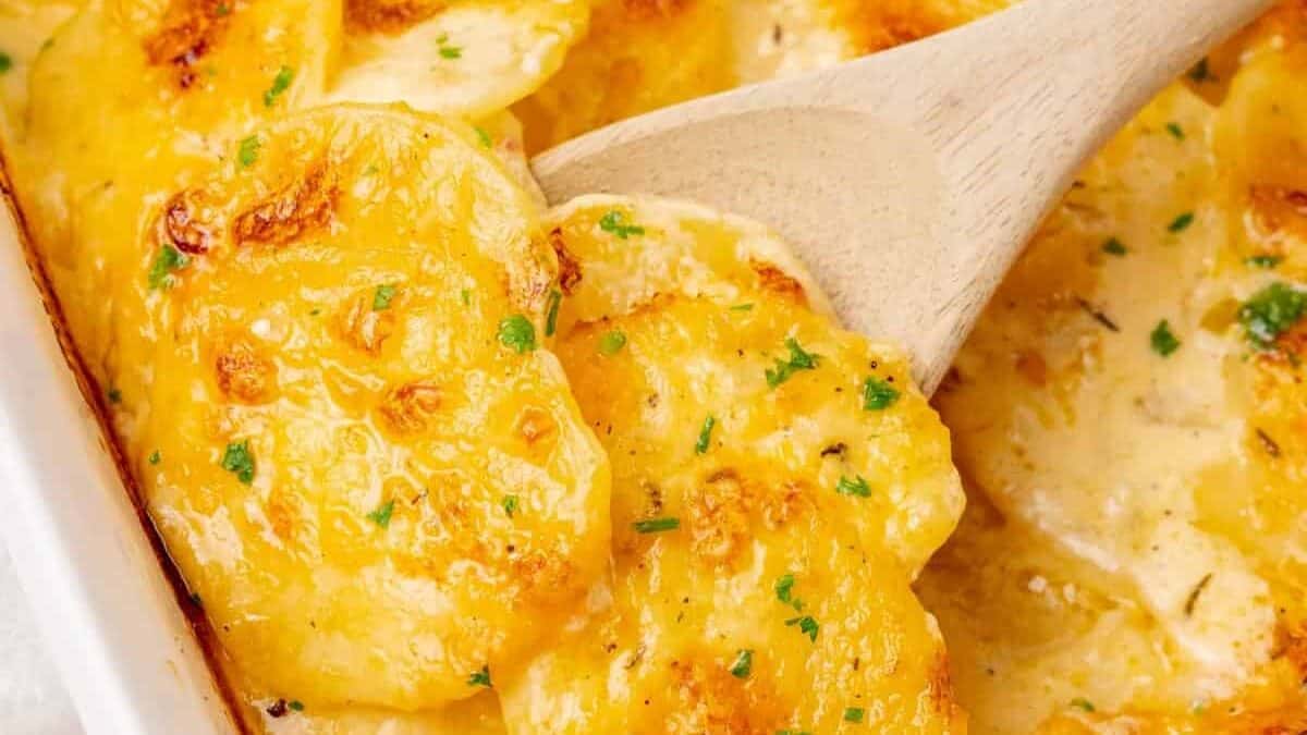 Cheesy potatoes in a casserole dish with a wooden spoon.