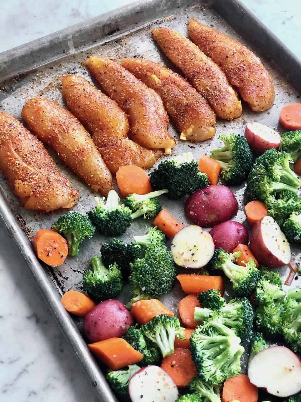 Tender roasted chicken and vegetables on a baking sheet.