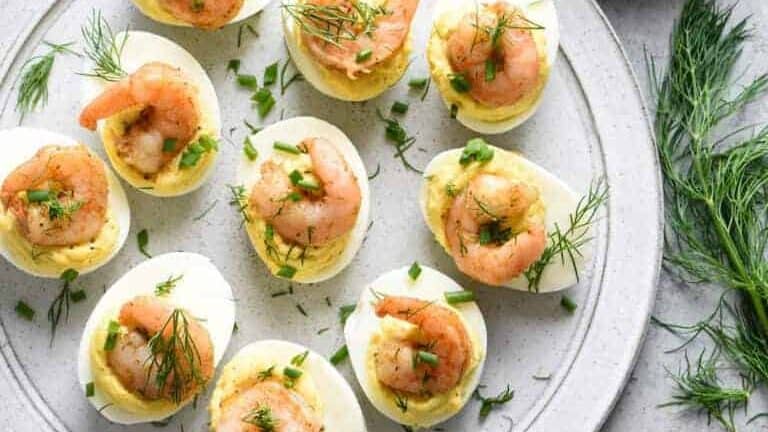 Deviled eggs with shrimp and dill on a plate.