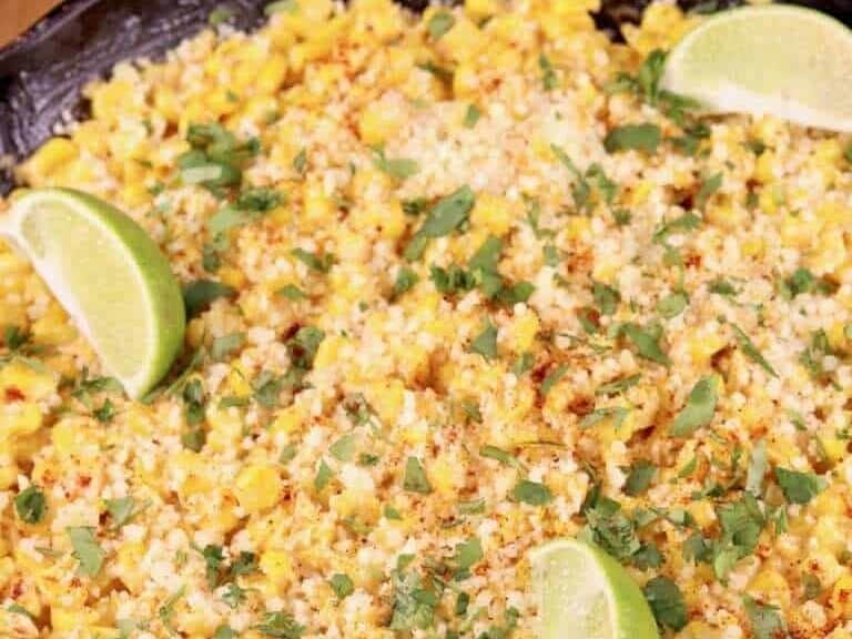 Corn on the cob in a skillet with lime wedges.