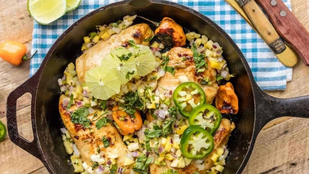 Mexican chicken in a skillet with corn and limes.