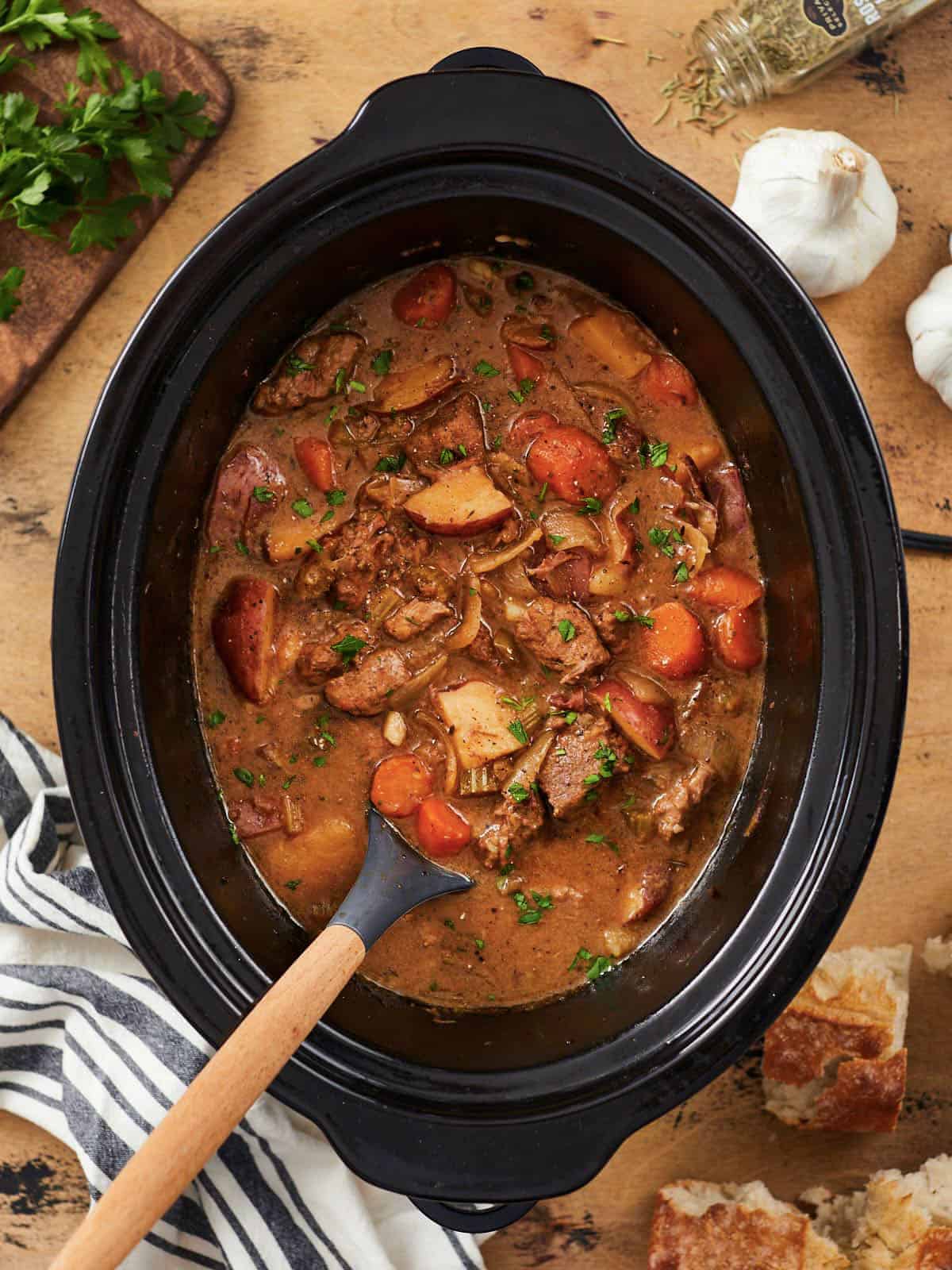 A hearty crock pot stew simmering with tender chuck steak, stirred gently with a wooden spoon.