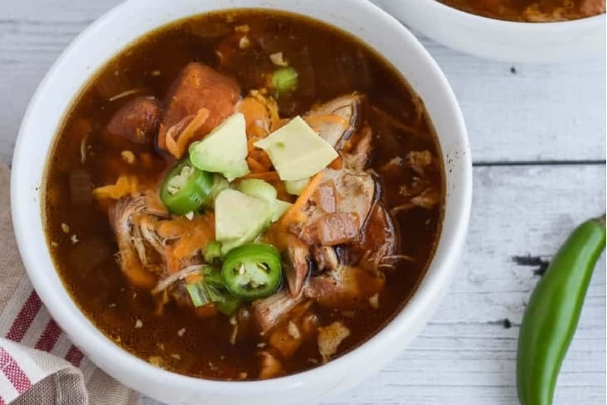 Two bowls of chicken tamale soup on a wooden table.