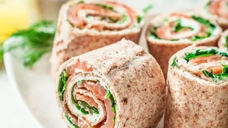 Salmon and spinach wraps on a white plate.