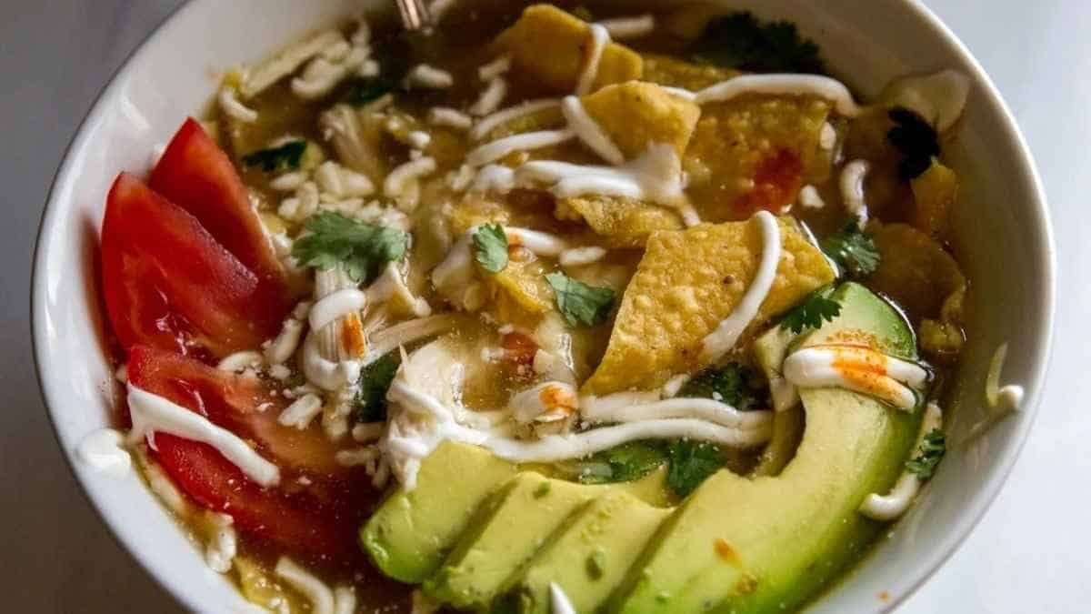 A bowl of mexican soup with avocado and tomatoes.