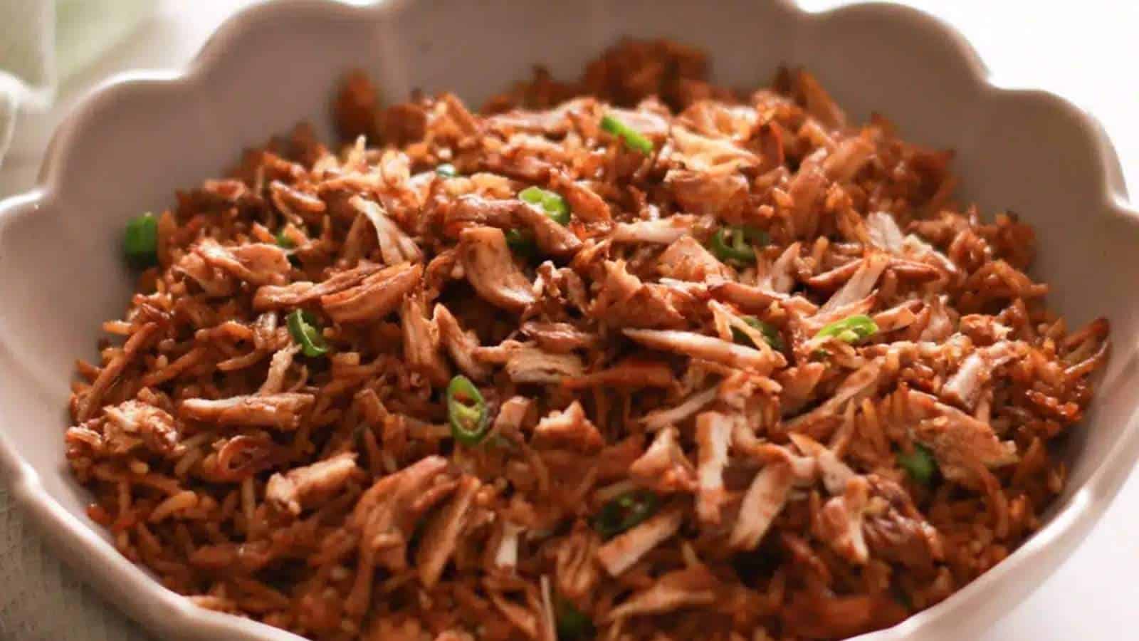 A bowl of rice with shredded chicken in it.
