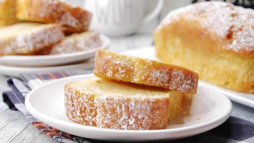 A slice of lemon pound cake on a plate with powdered sugar.