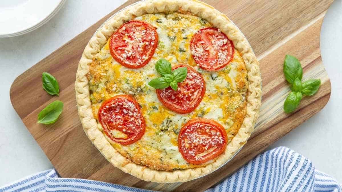 A quiche with tomatoes and basil on a cutting board.