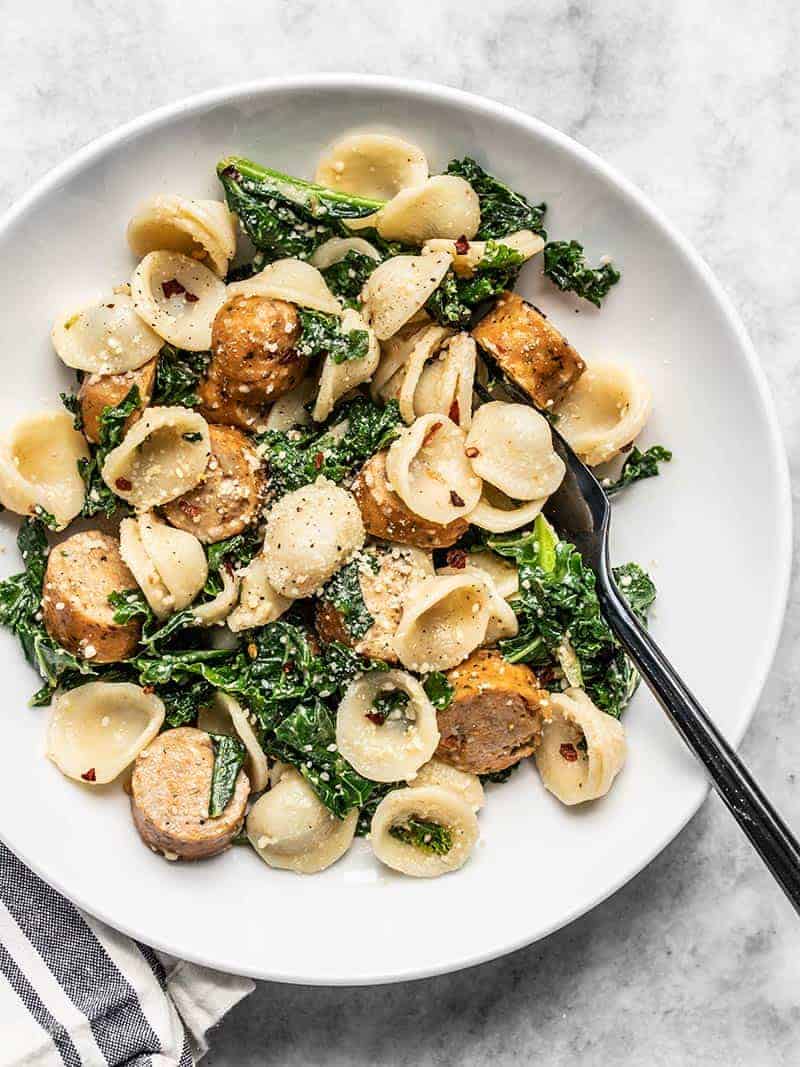 Sausage pasta with kale in a white bowl.