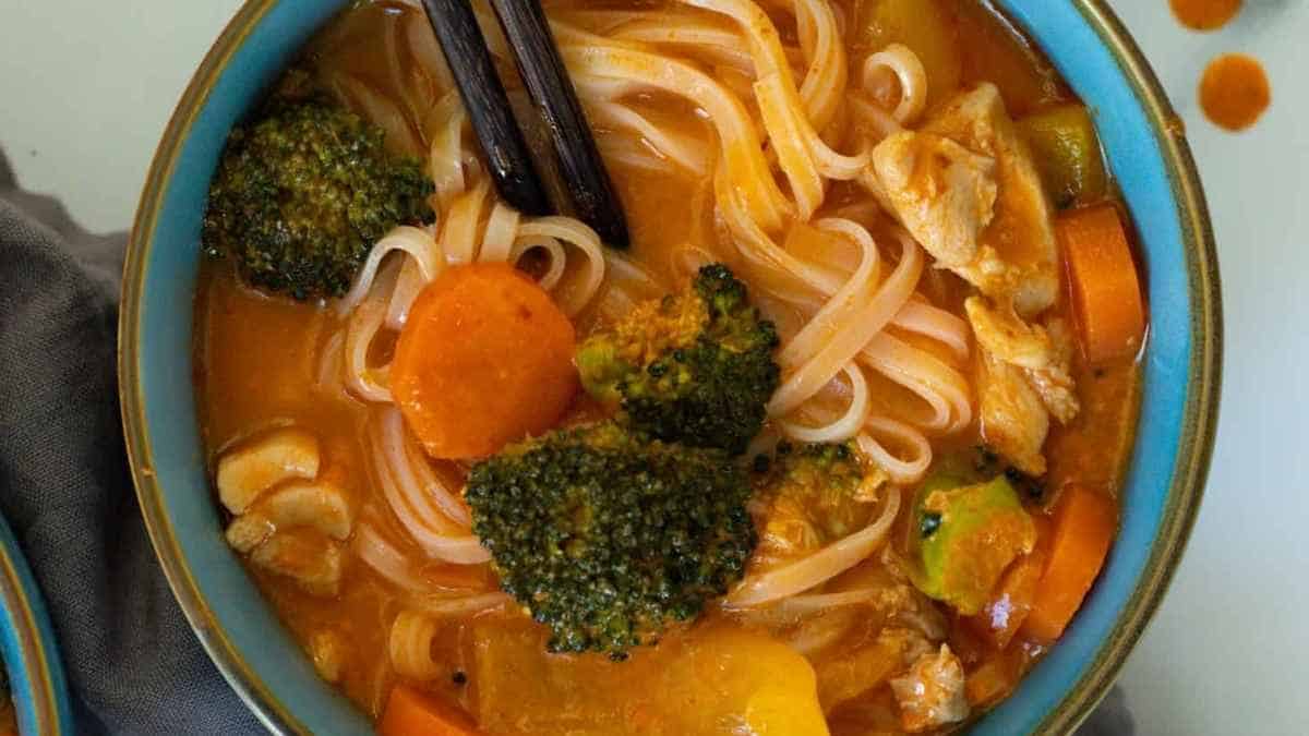 A bowl of chicken noodle soup with broccoli and carrots.