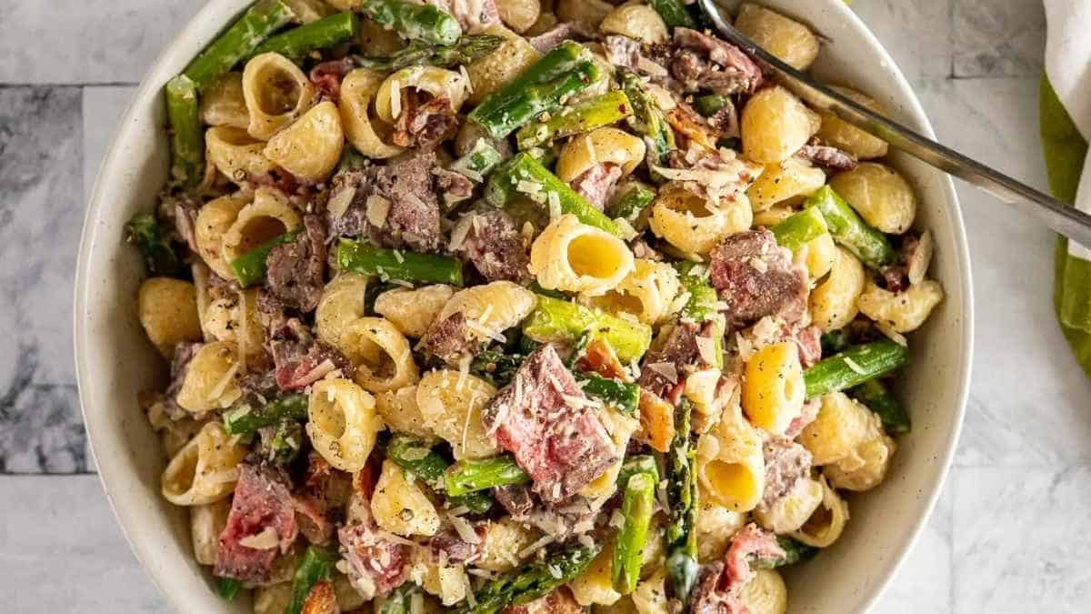 Pasta with meat and asparagus in a white bowl.