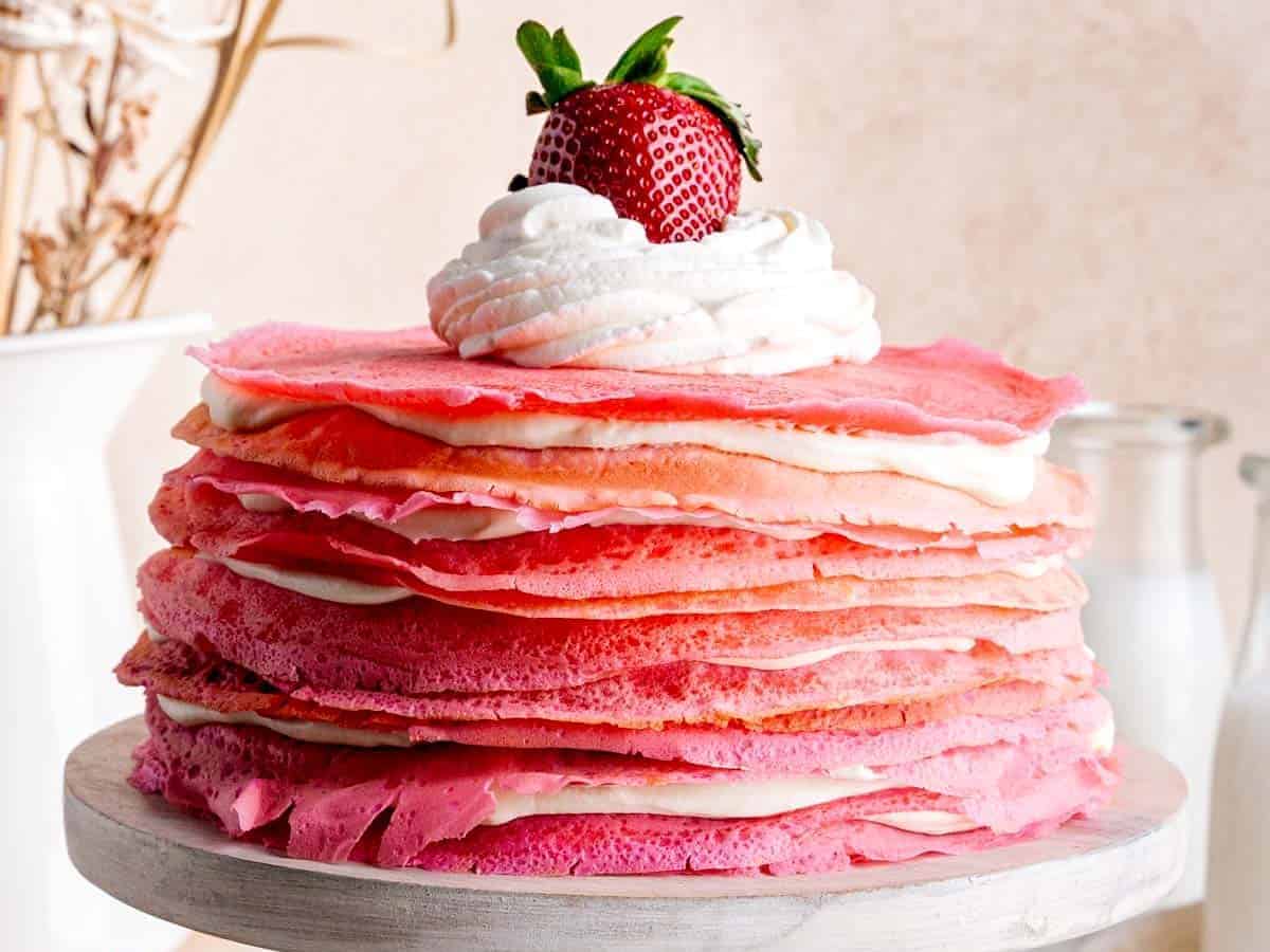 Strawberry crepe cake with whipped cream and strawberries on a cake stand.