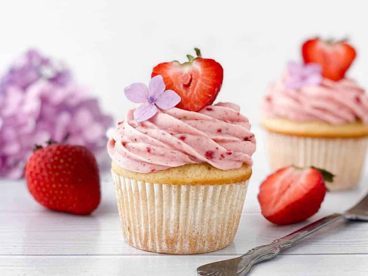 Two cupcakes with strawberries and a fork on a wooden table.