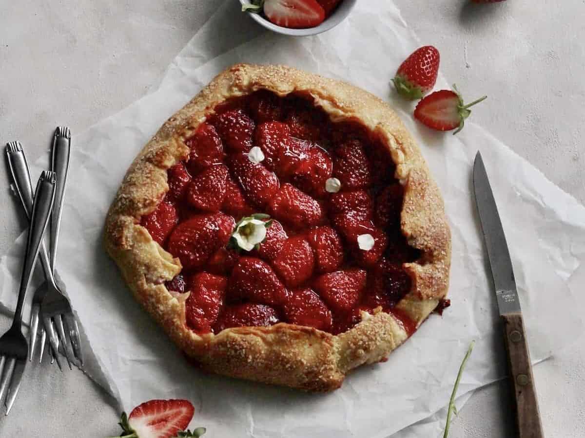 A strawberry galette on a piece of paper with a knife and fork.