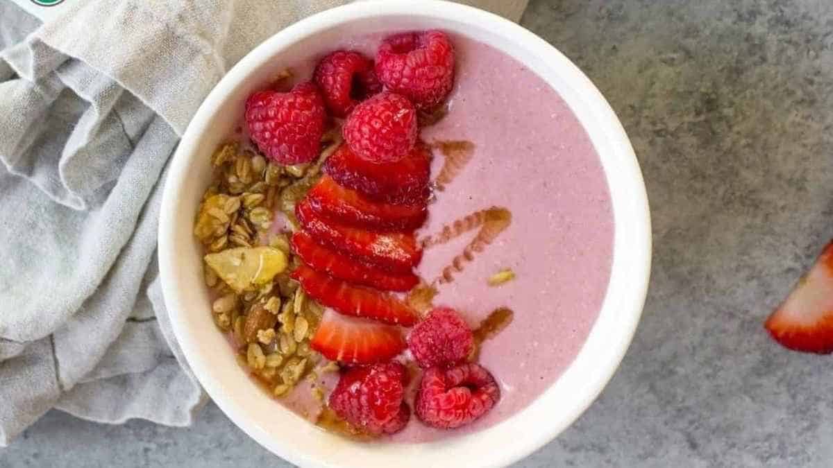 A bowl of strawberry and granola smoothie with raspberries and granola.