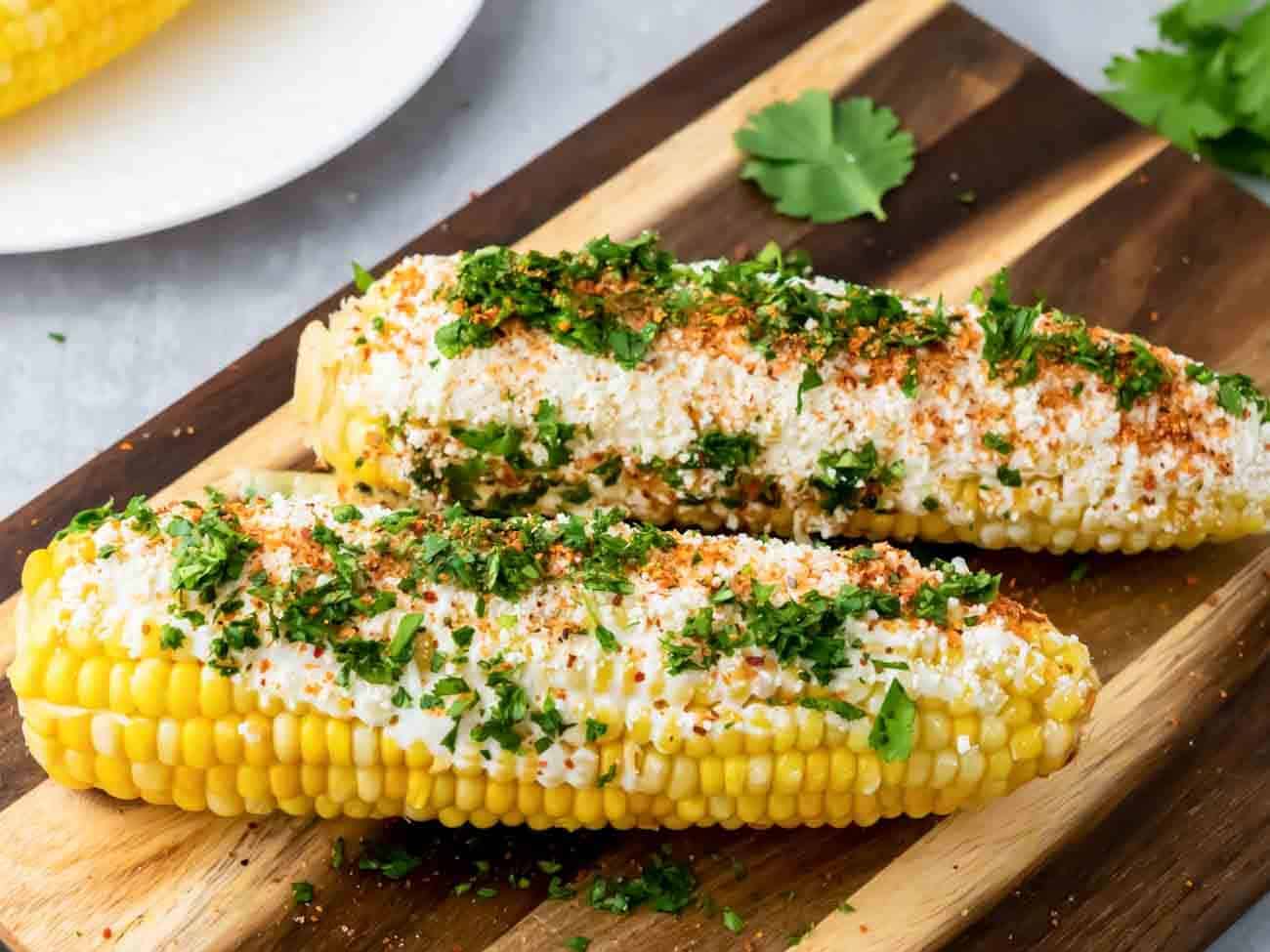 Two corn on the cob on a wooden cutting board.