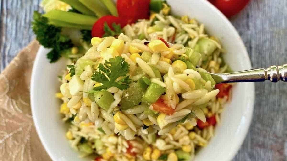 A spoonful of a salad with corn, tomatoes, and cucumbers.