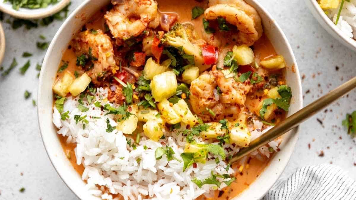 A bowl of shrimp curry with rice and vegetables.