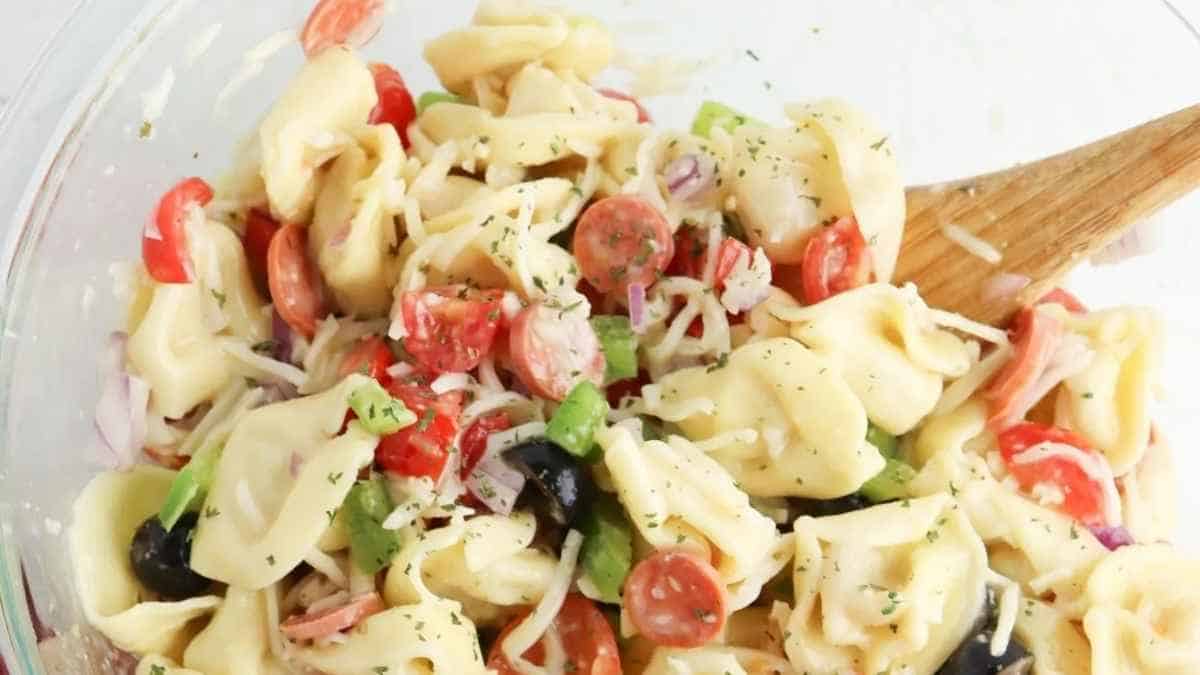 Tortellini salad in a bowl with a wooden spoon.