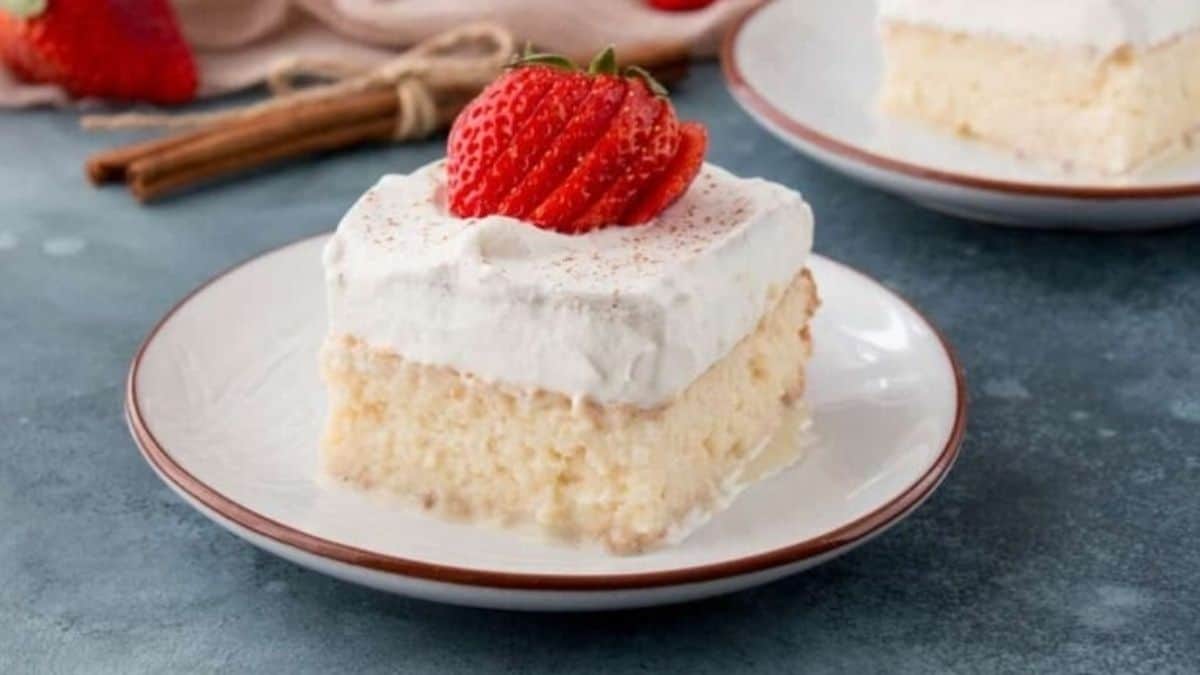 A slice of white cake on a plate with a strawberry on top.