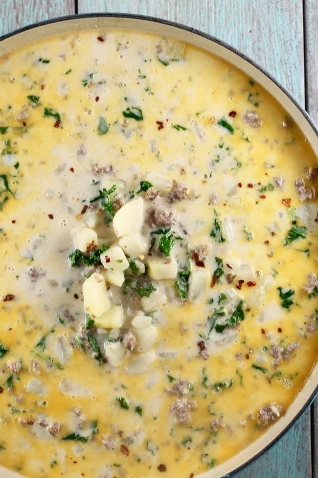         Cheesy potato soup with sausage in a pan on a wooden table.