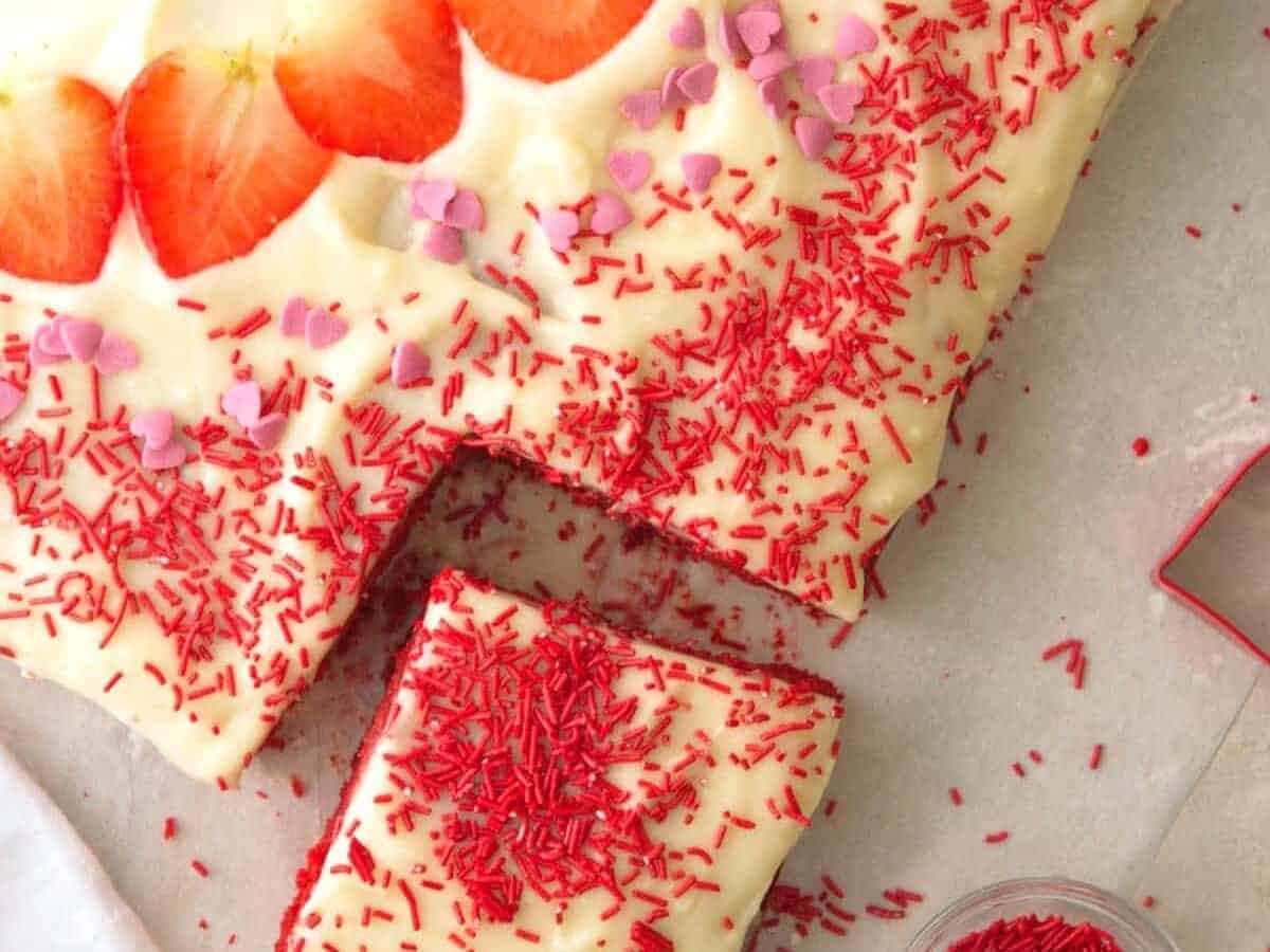 A slice of red velvet cake with strawberries and icing.