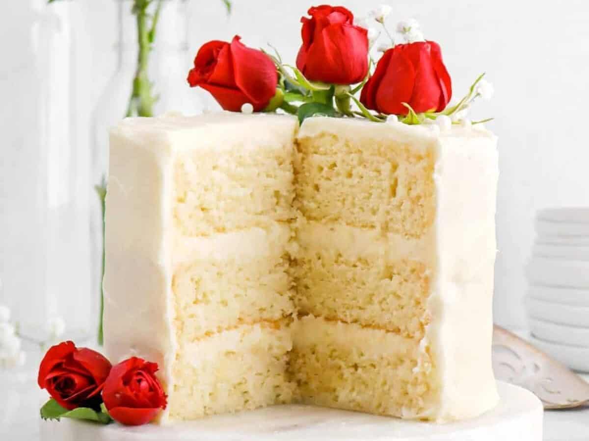A white cake with red roses on a white plate.