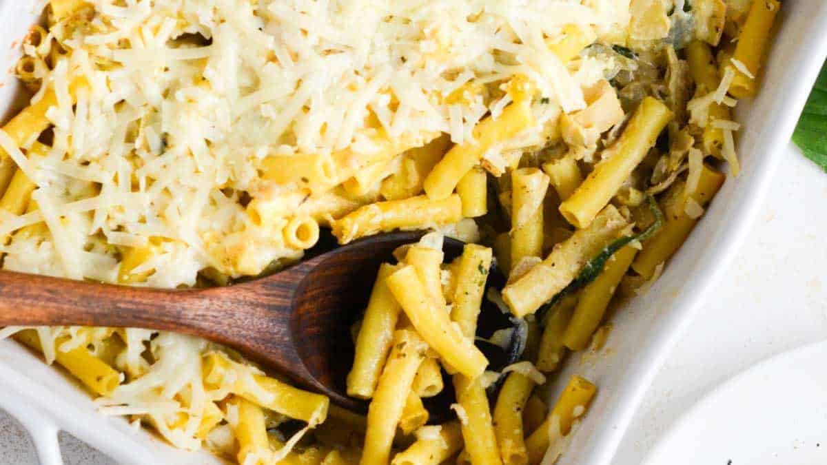 Cheesy spinach and artichoke pasta in a white dish with a wooden spoon.