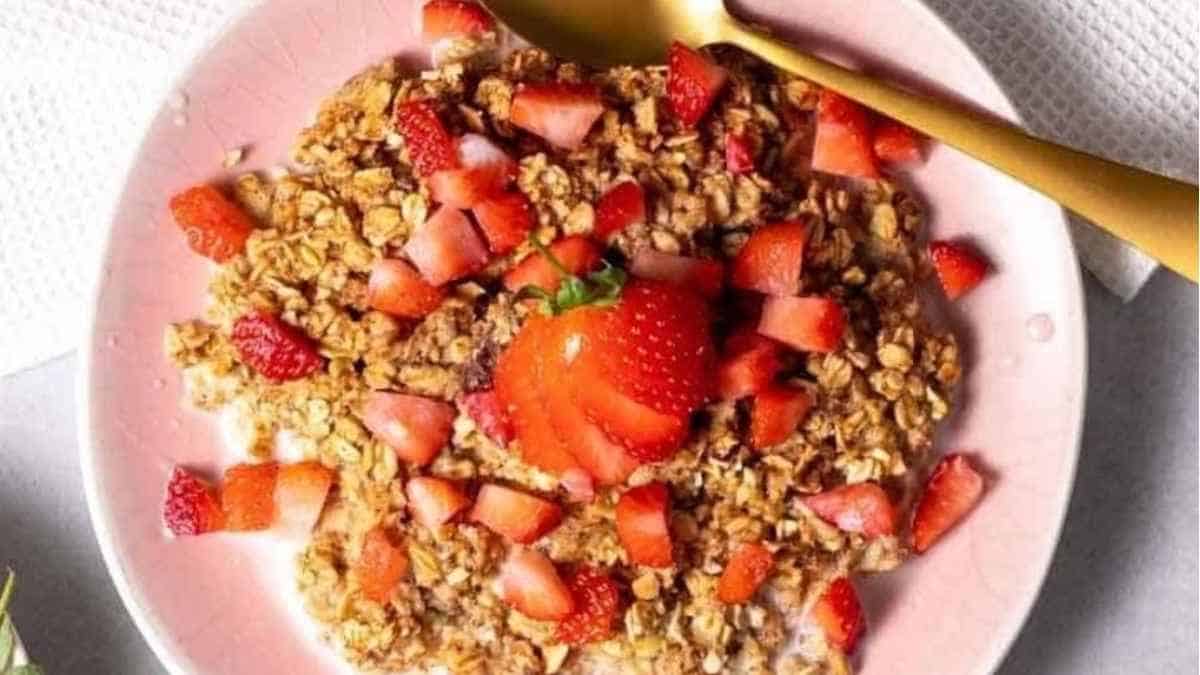 A pink plate with granola and strawberries on it.