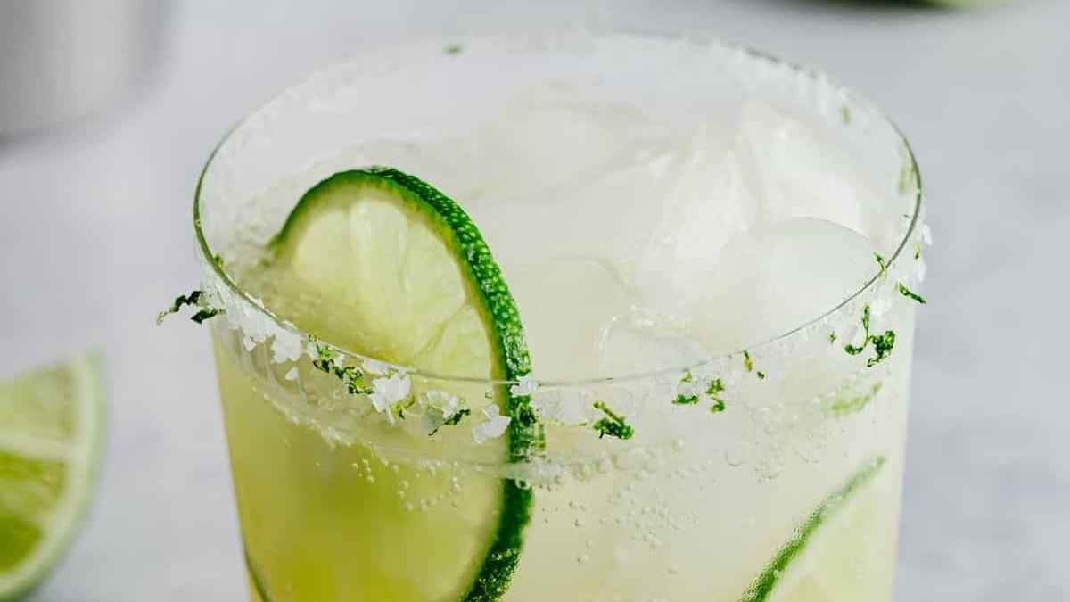 A lime margarita in a glass with a slice of lime.