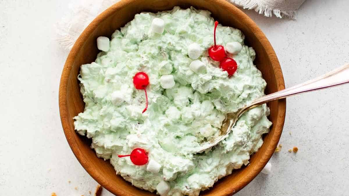 A bowl of green ice cream with cherries in it.