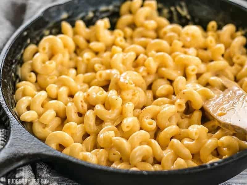 Macaroni and cheese in a skillet with a wooden spoon.