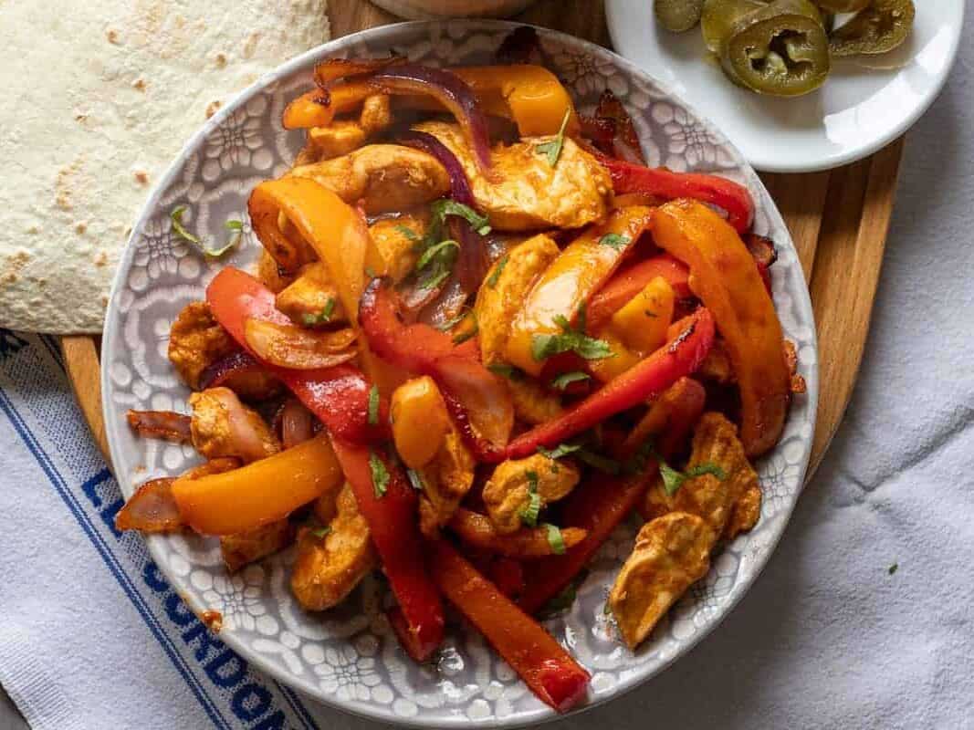 Chicken fajitas on a plate with tortillas and salsa.