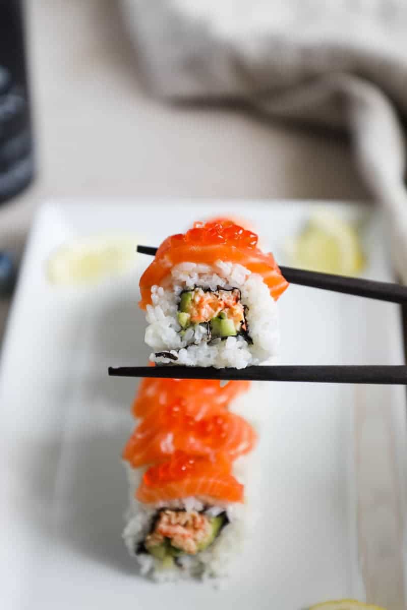 Salmon sushi on a white plate with chopsticks, a delicious and visually appealing dish.