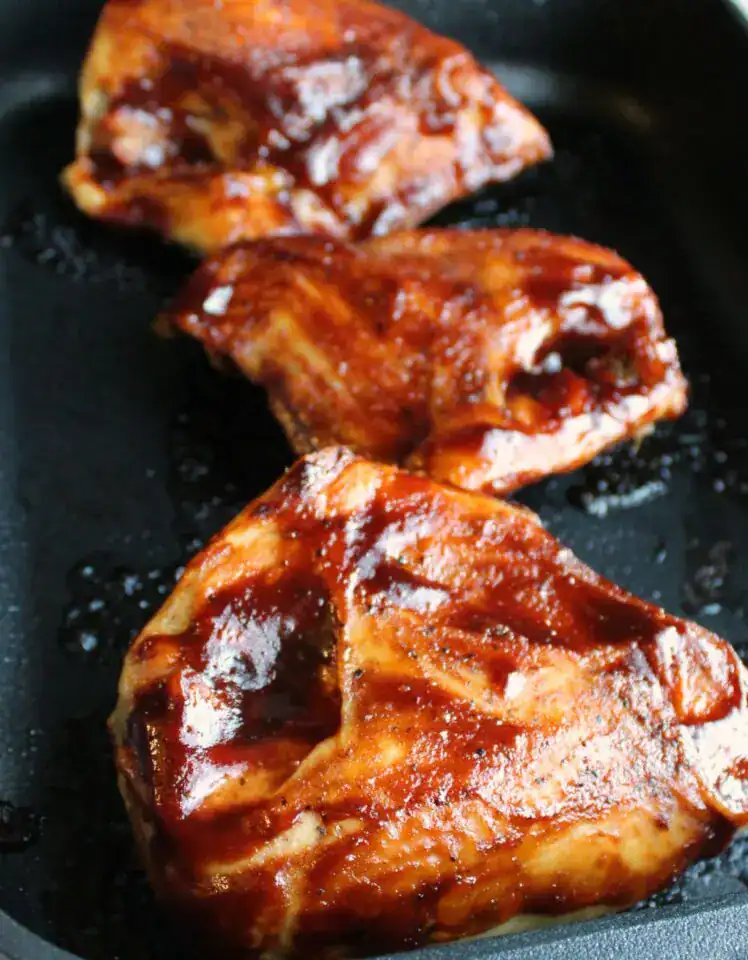 Bone-in chicken breasts cooked in a skillet with luscious BBQ sauce.