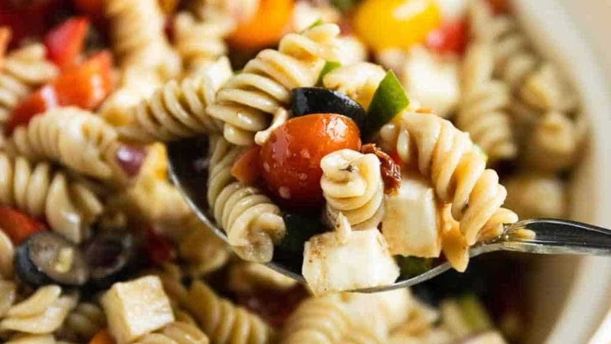 A spoonful of pasta salad with tomatoes and vegetables.