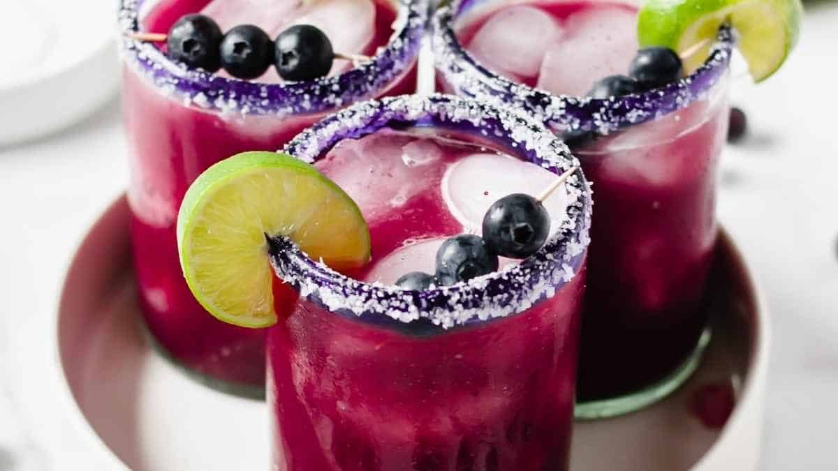 Three margaritas with blueberries and limes on a plate.