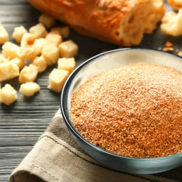 Glass bowl with bread crumbs and baguette on wooden table