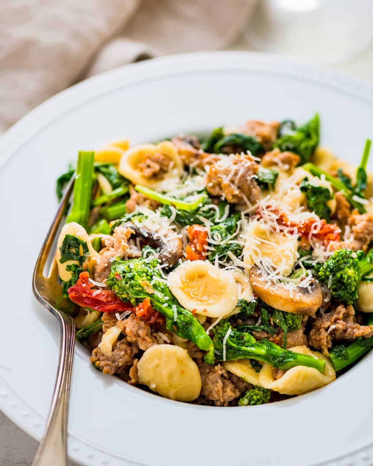 A plate of pasta with ground sausage and vegetables on it.