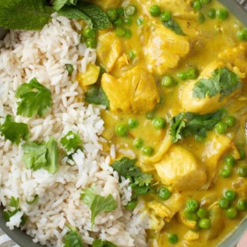 An individual enjoying an easy dinner by holding a bowl of flavorful chicken curry with rice and peas.