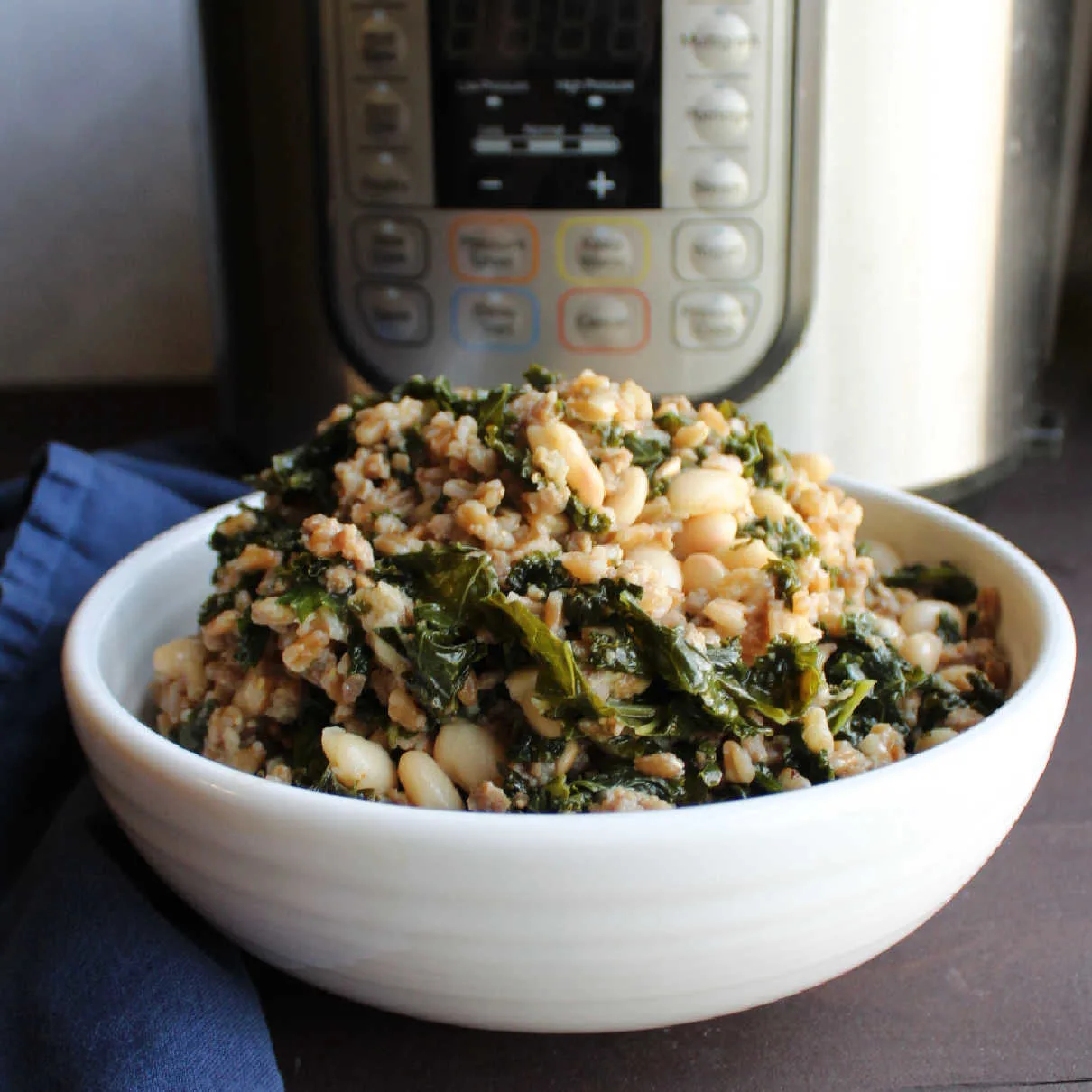 A bowl of kale, white beans, and ground sausage in front of an instant pot.