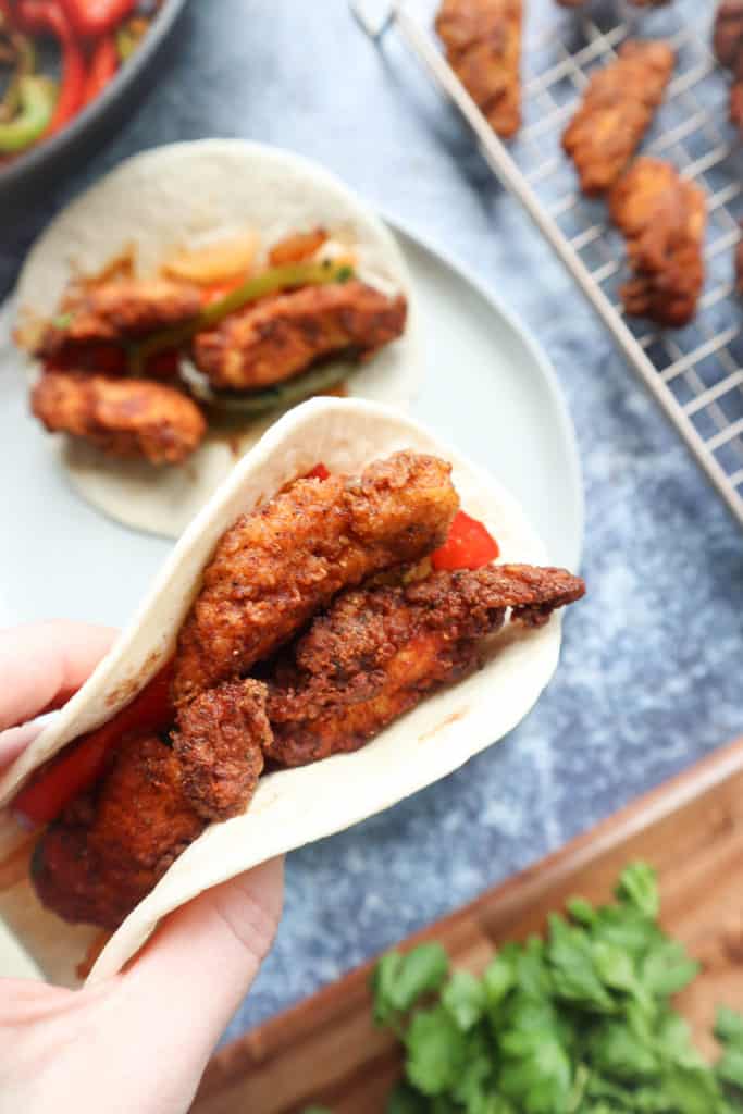 A person holding a taco with crispy fried chicken in it, showcasing delectable chicken tender recipes.